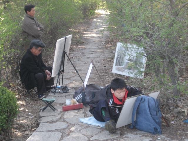 Taiteilijat työssään Pjongjangin puistossa. Etummaisen piirtäjän tunistaa huivista pioneeriksi. Kaikki kouluikäiset kuuluvat pioneereihin.