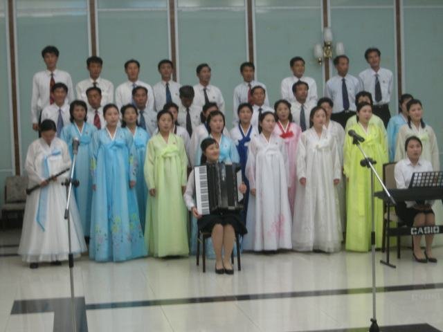 Pohjoiskorealaisen spa-hotellin (!) henkilökunta esittää musiikkia Kim Il Sungin kunniaksi. Turistit kuuntelivat esitystä kiltisti. Naisilla on päällään kansallispuvut.