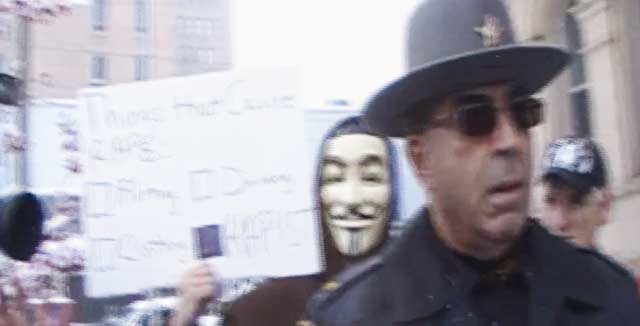 Anonymousin maskiin pukeutunut henkilö kysyy haastattelun taustalla, mikä aiheuttaa raiskauksen. Vastaus on raiskaaja.