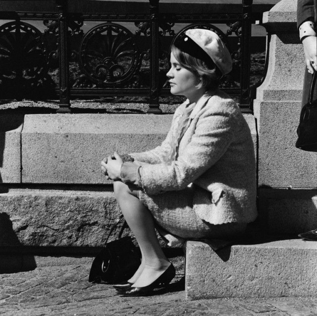 Nainen istuu vapunpäivänä ylioppilaslakki päässä Aleksanteri II:n patsaan juurella.